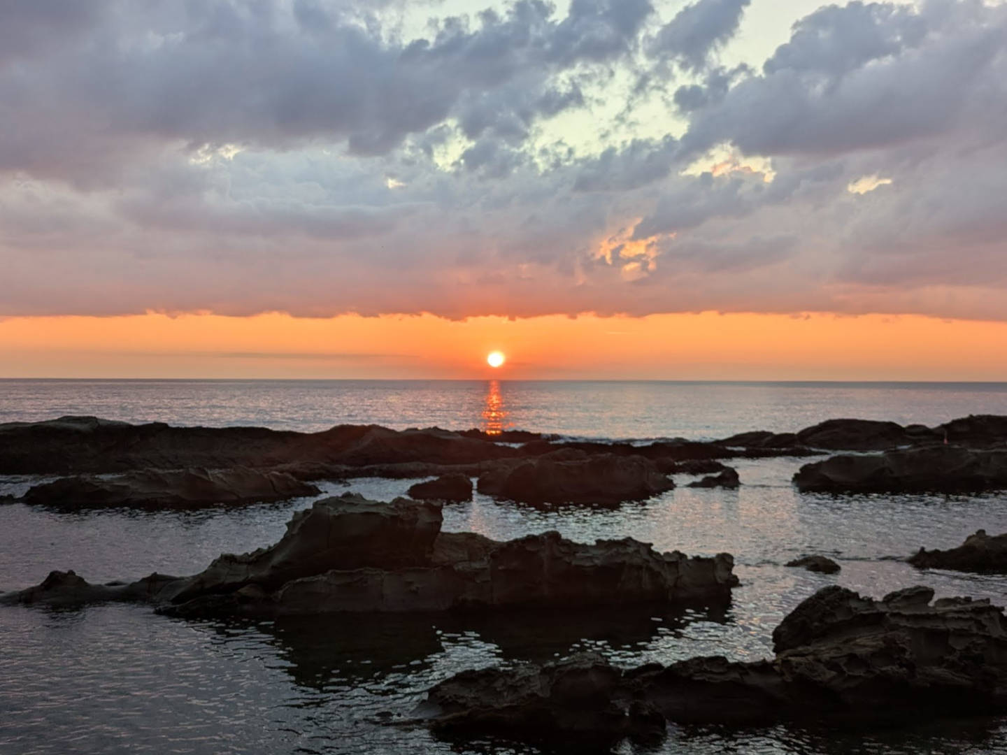 はりいしゃ近くの海に沈む夕日と岩礁